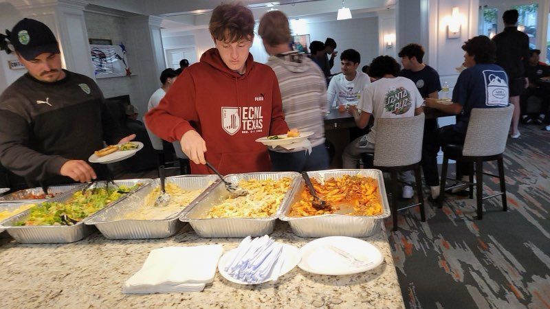 A group of people are standing around a buffet table eating food.