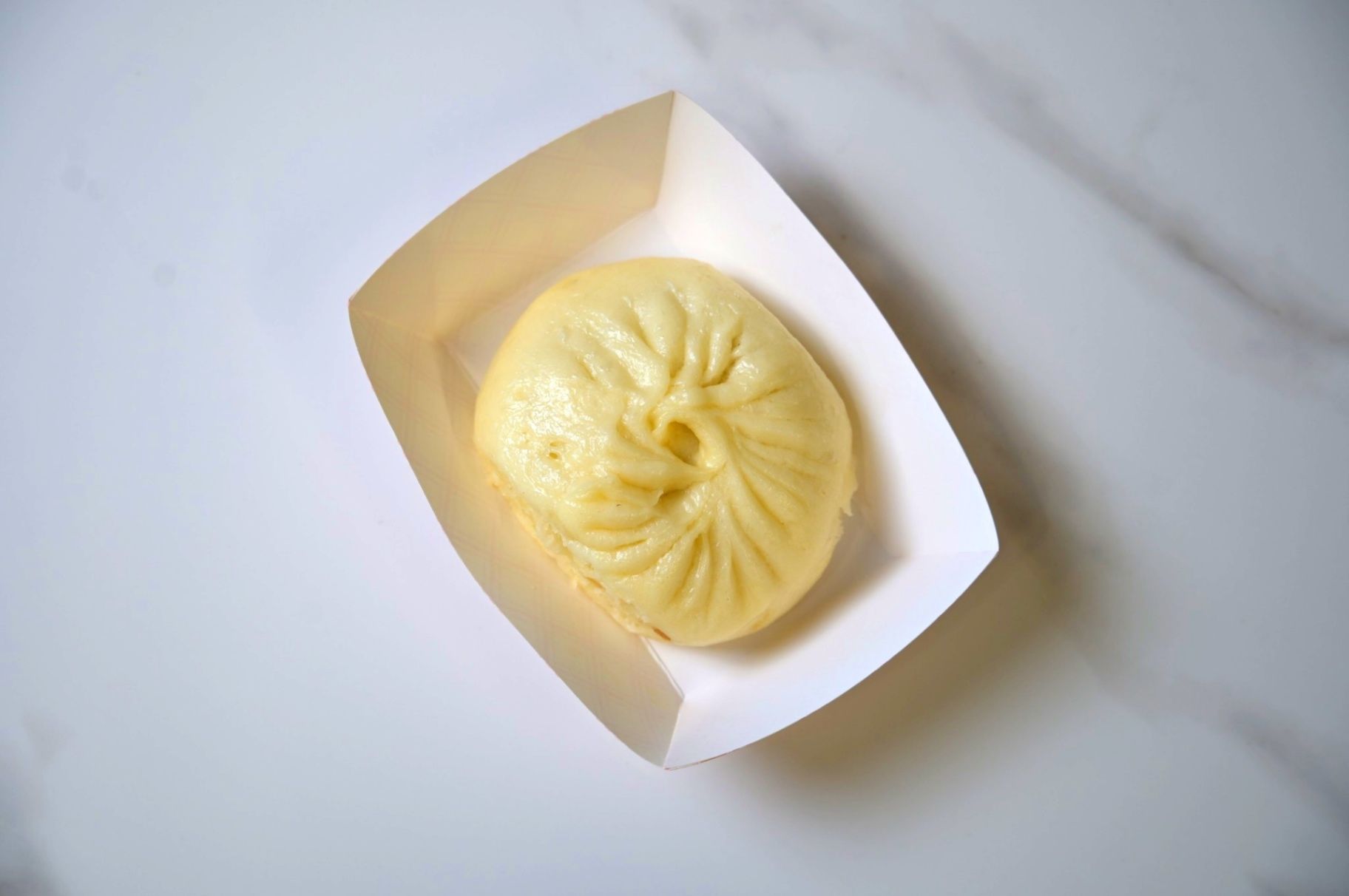 Steamed bun in a white paper tray on a light marble surface