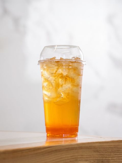 Tall iced orange drink in a clear plastic cup on a wooden table, against a light background