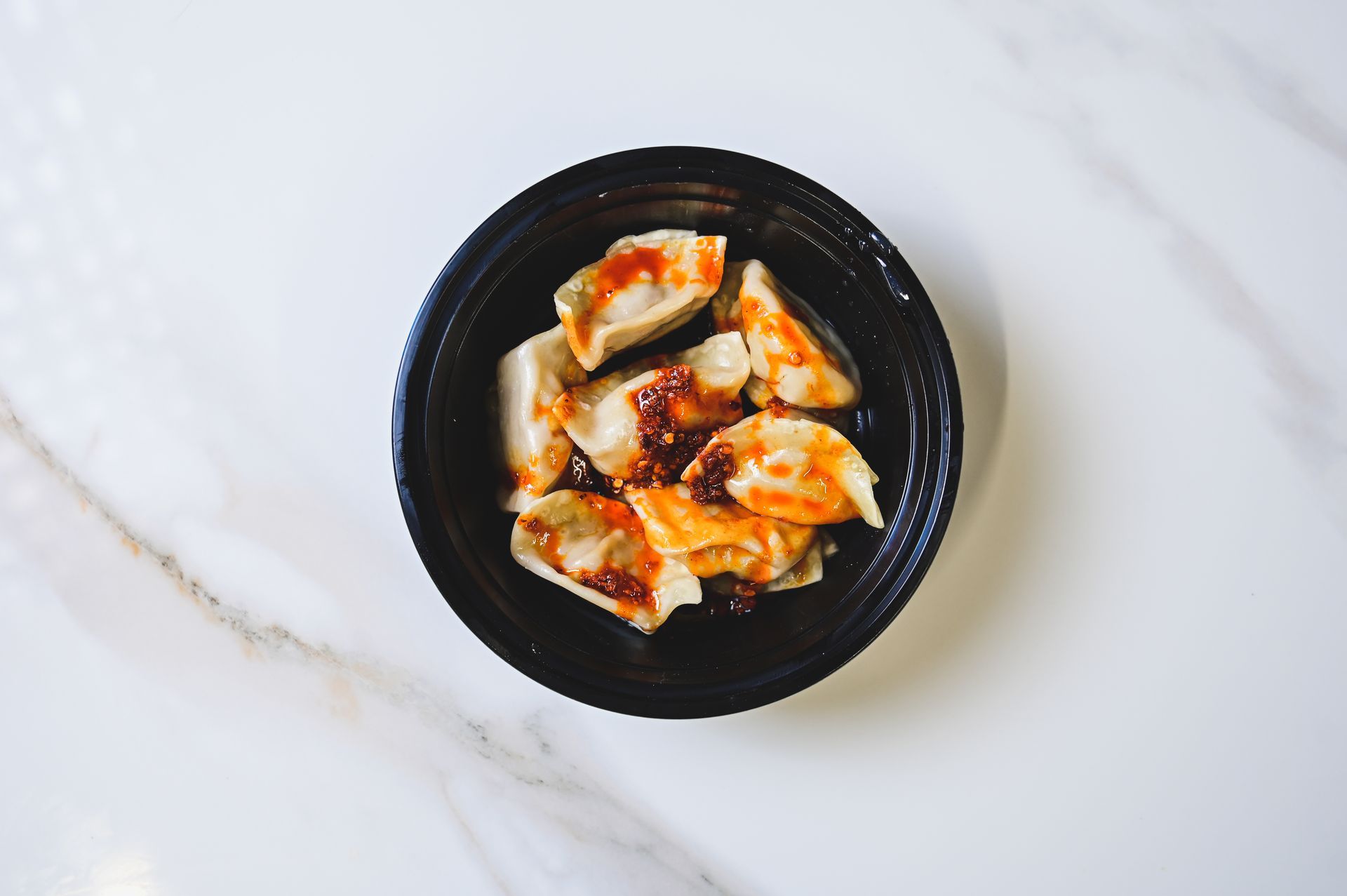 Black bowl of dumplings topped with red sauce on a white marble surface