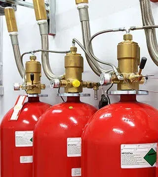 Red fire suppression tanks with brass valves and metal hoses in a utility room