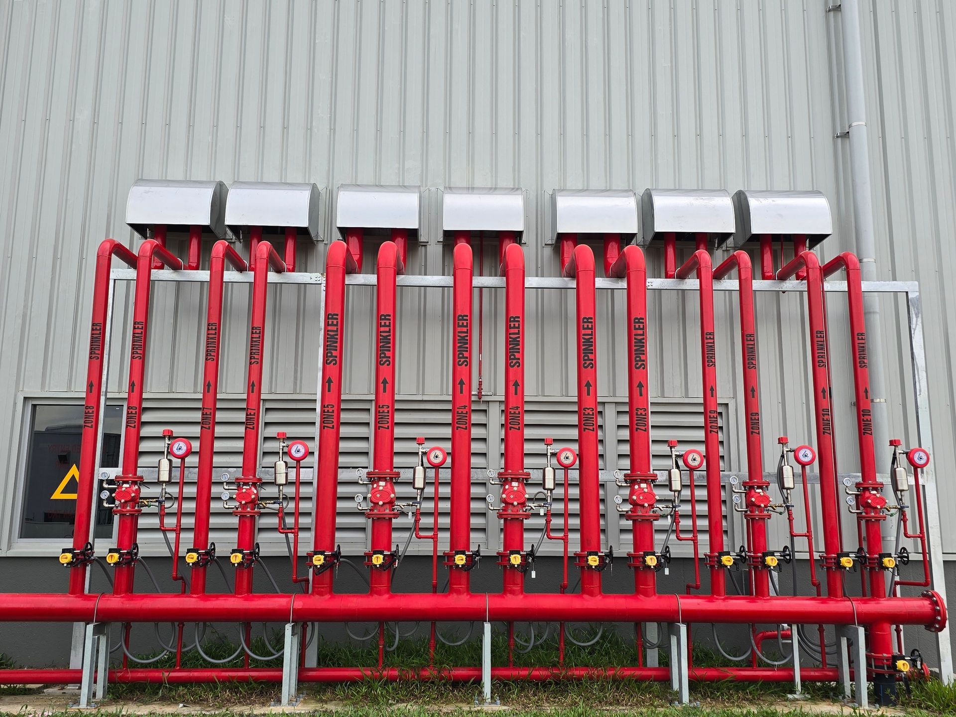 Row of red industrial valves and pipes mounted on a metal wall outdoors