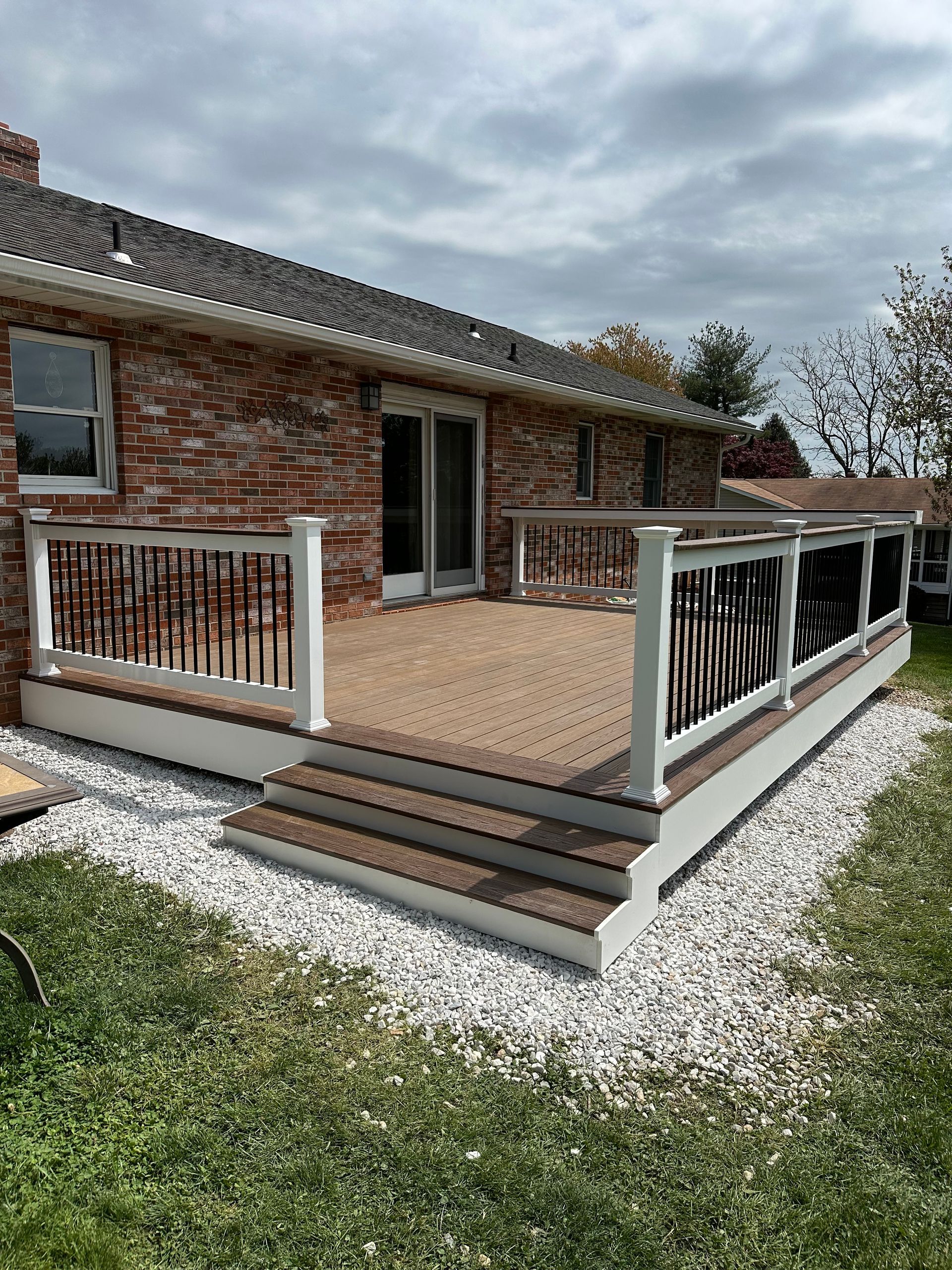 A large deck with stairs is in front of a brick house.