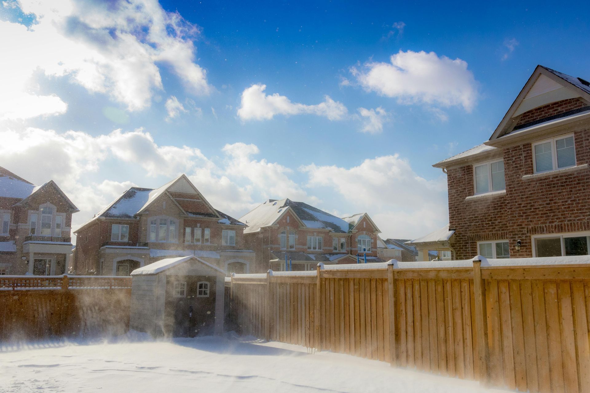 A wooden fence is surrounded by snow covered houses in a residential area.
