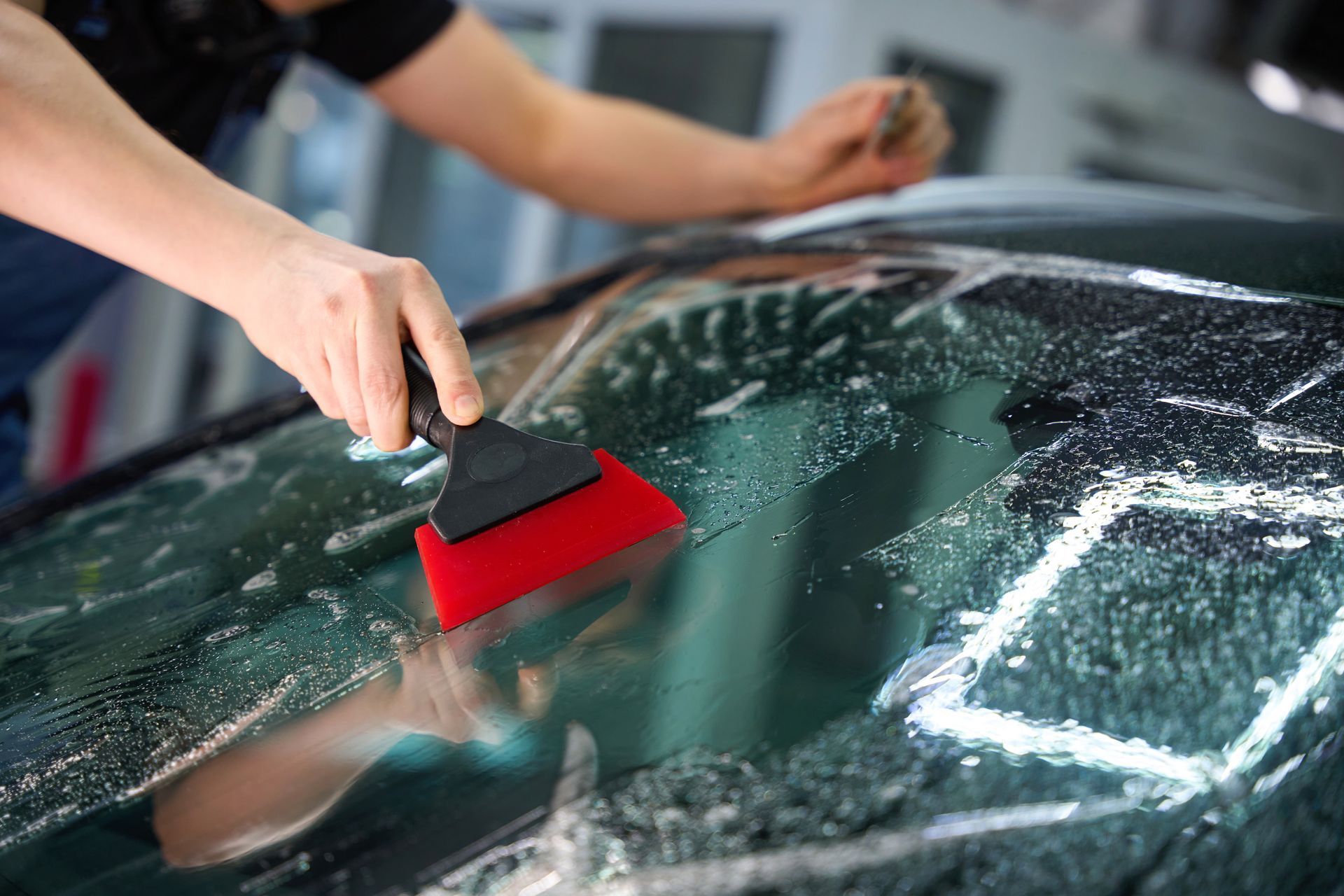 Worker Smoothing Protective Film on a Car Windshield