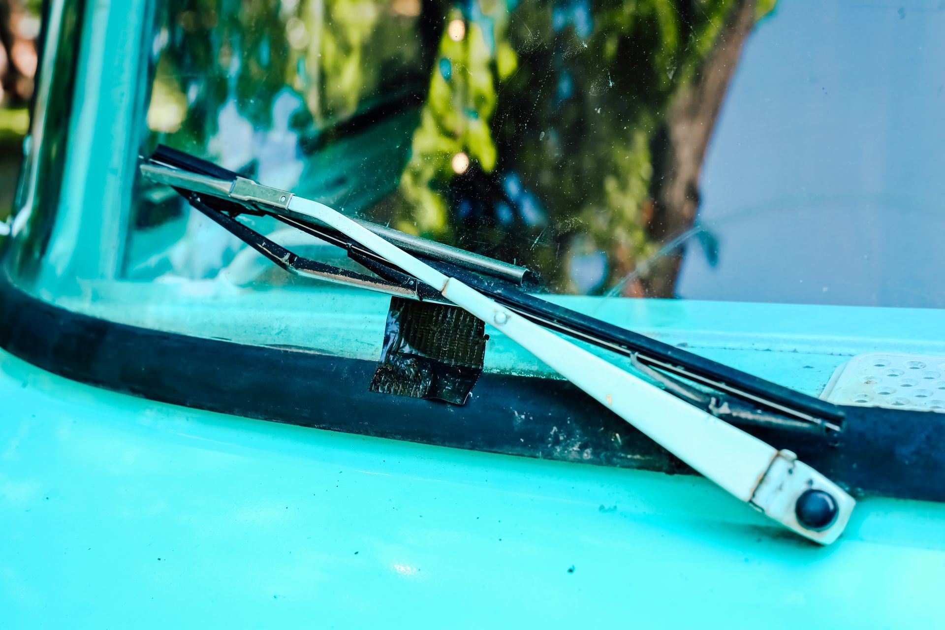 Windshield wiper resting on green vintage truck parked under a tree in bright daylight Windshield wiper resting on green vintage truck parked under a tree in bright daylight