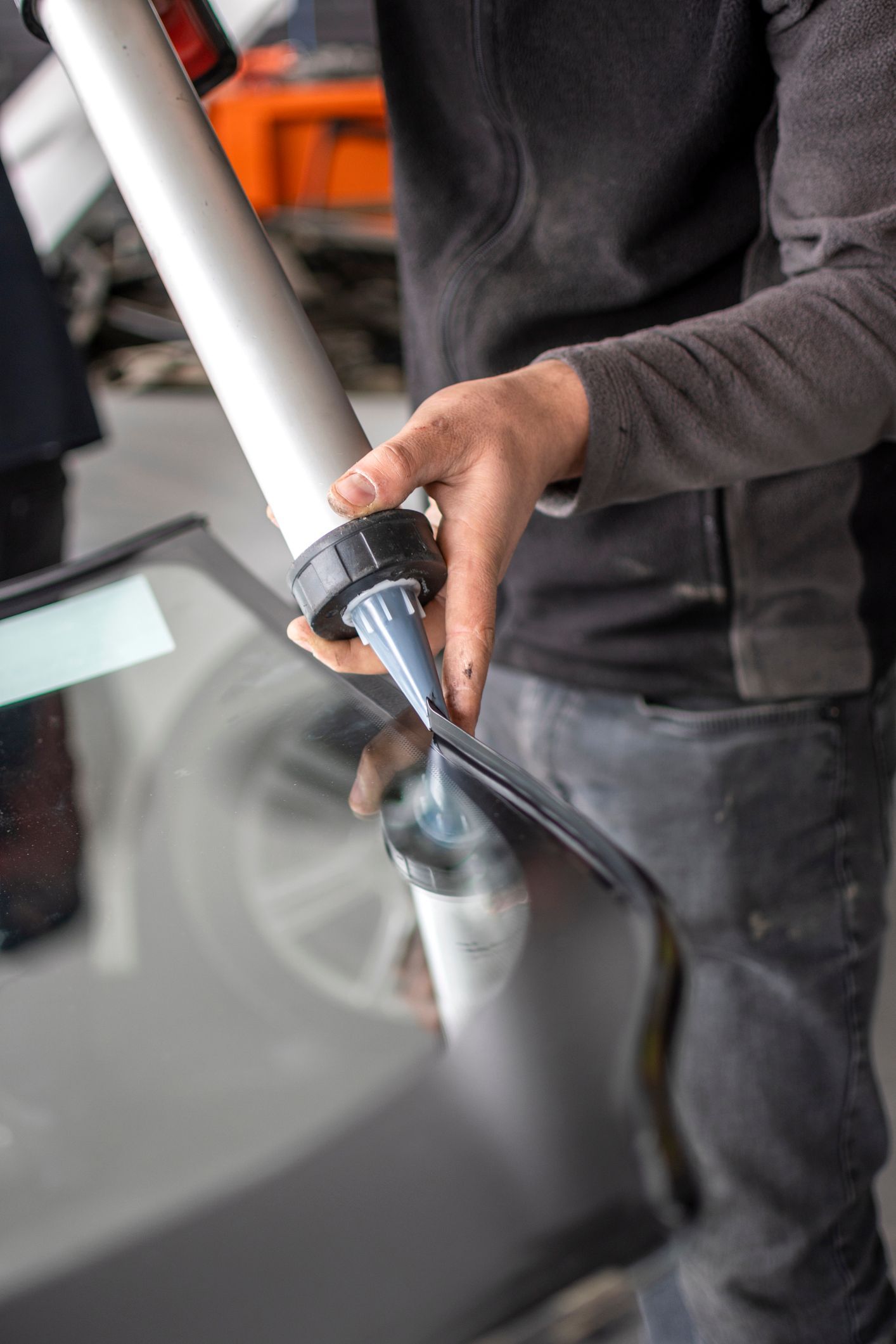 Person applying sealant to a car windshield with a caulking gun in a workshop.