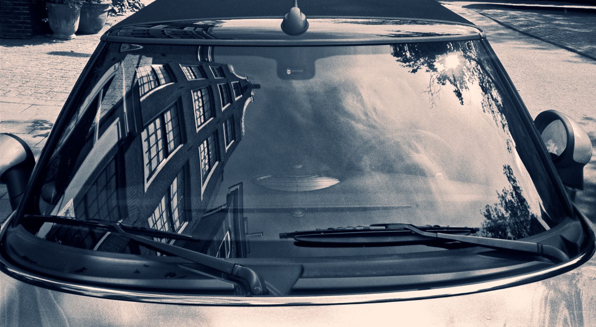 Windshield of a convertible reflecting a building with windows, in black and white.