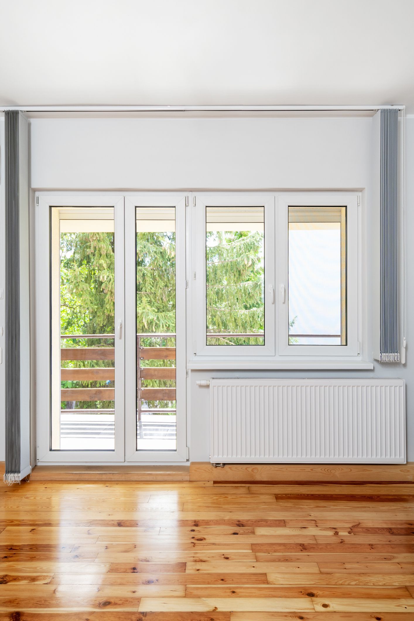 Bright room with balcony doors and window, light wood floor, white walls, and radiator.