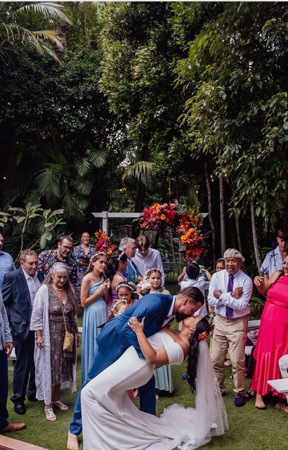 Wedding couple kissing under a floral arch as guests watch outdoors