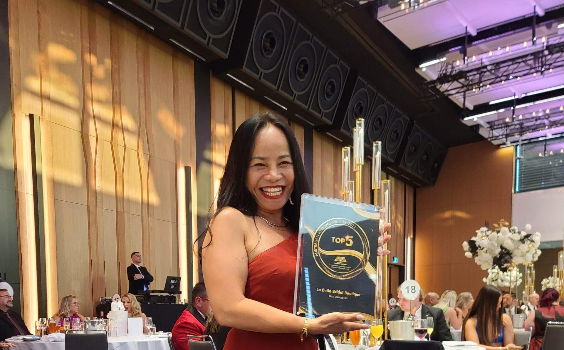 A woman in a red dress is holding a trophy in a large room.