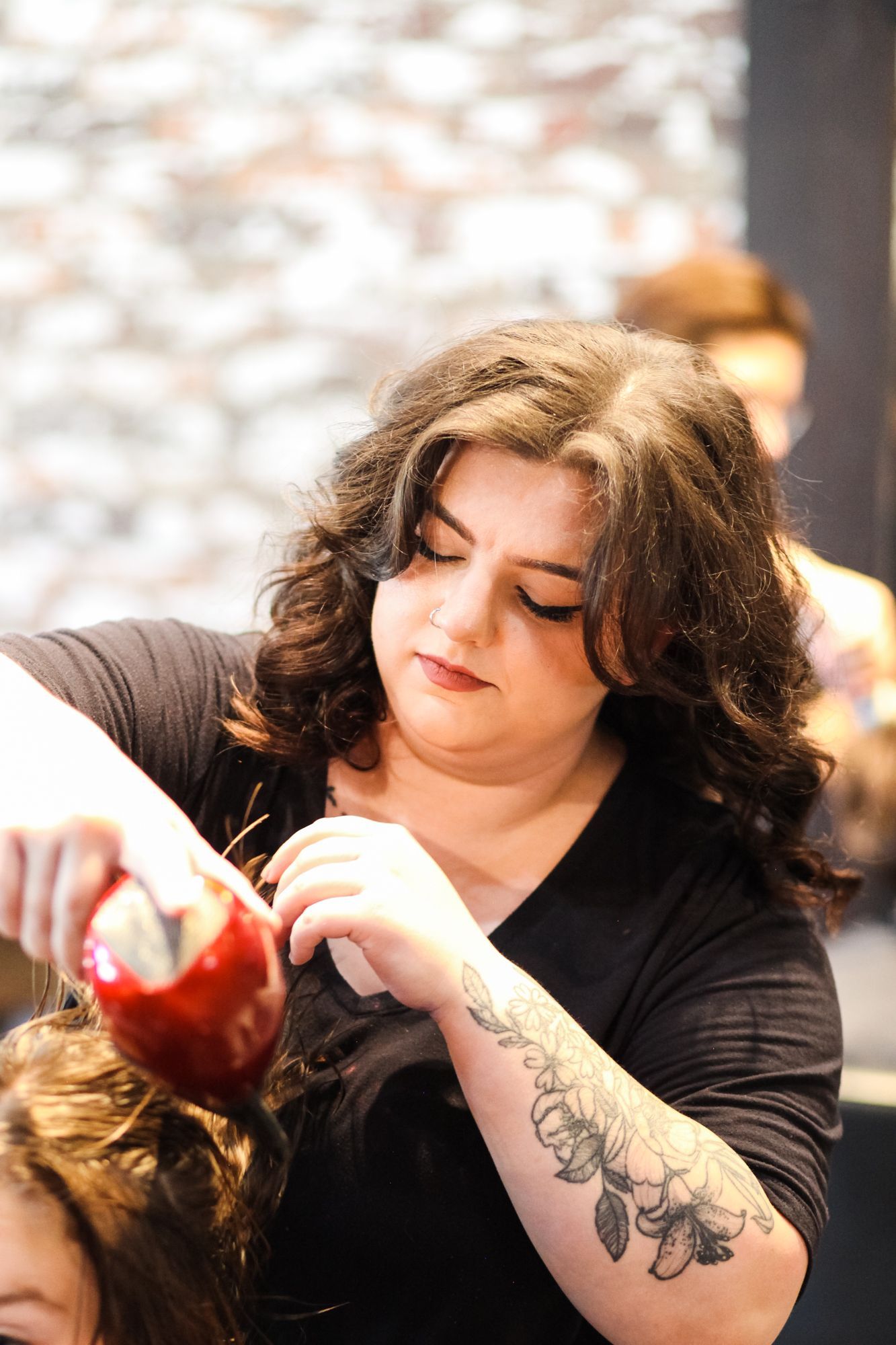 Hairdresser styling hair with spray bottle, arm tattoo visible.