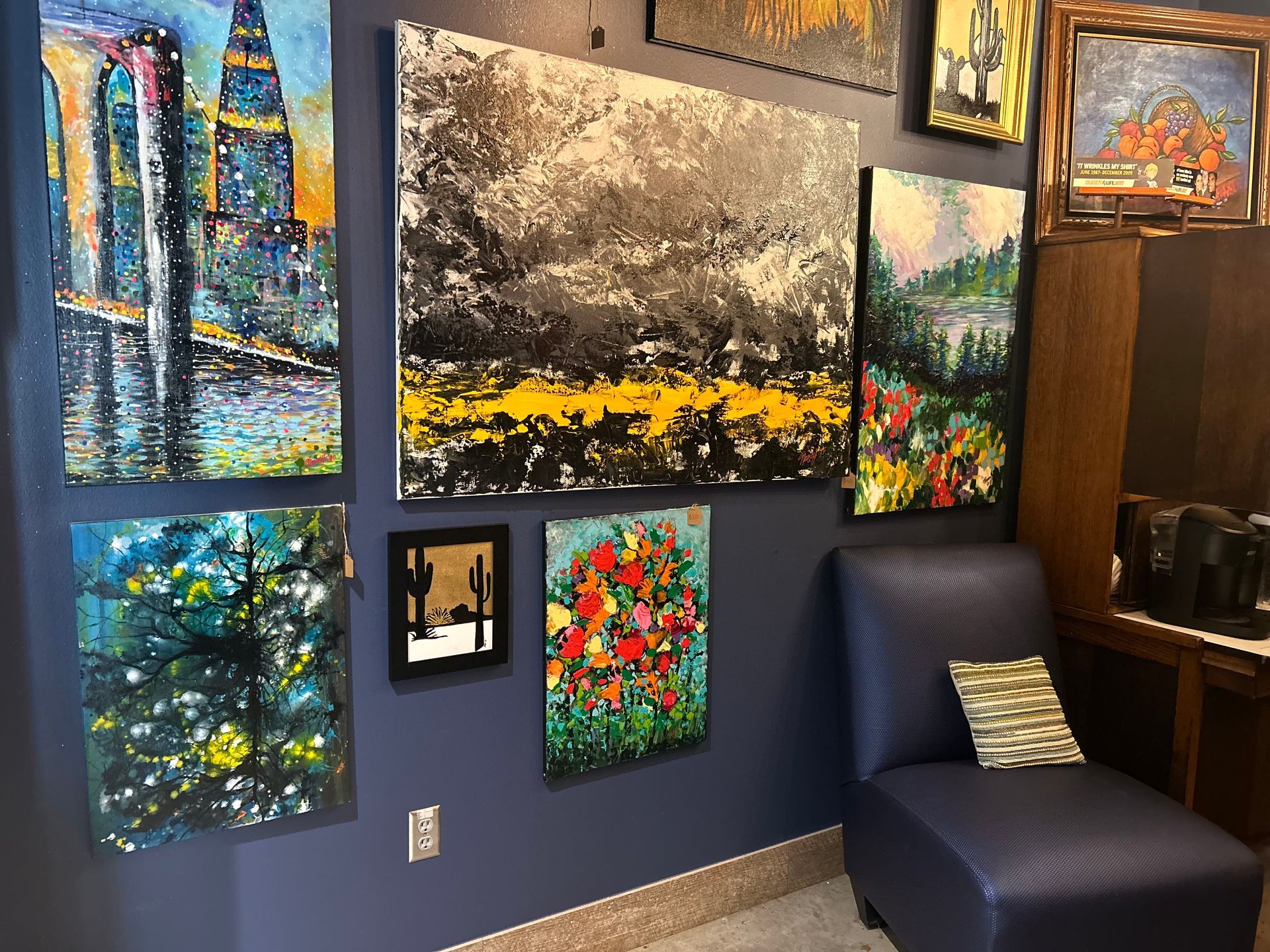 A gallery wall displaying colorful abstract paintings, near a blue armchair.