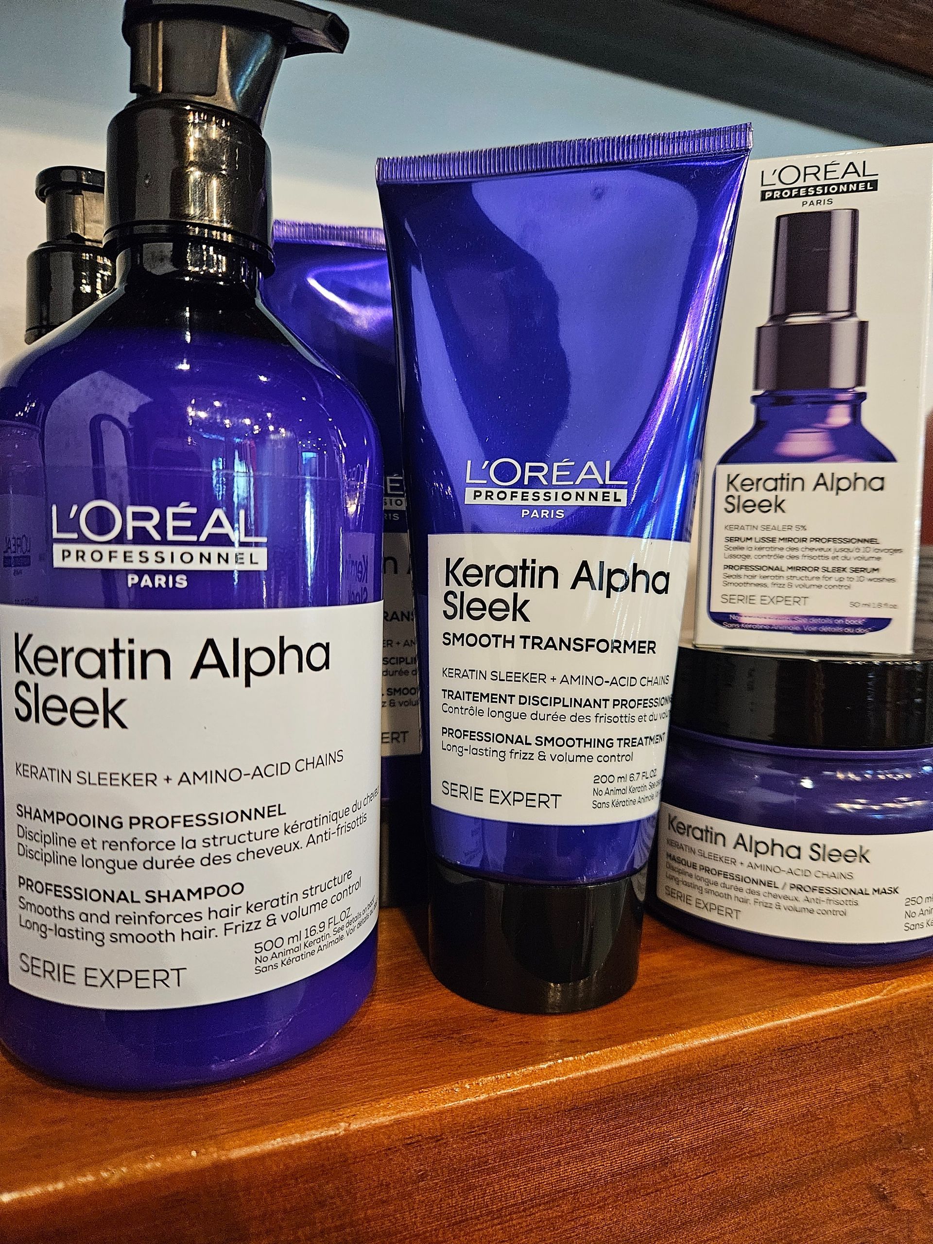 Four L'Oréal Keratin Alpha Sleek haircare bottles and tube on a wooden surface
