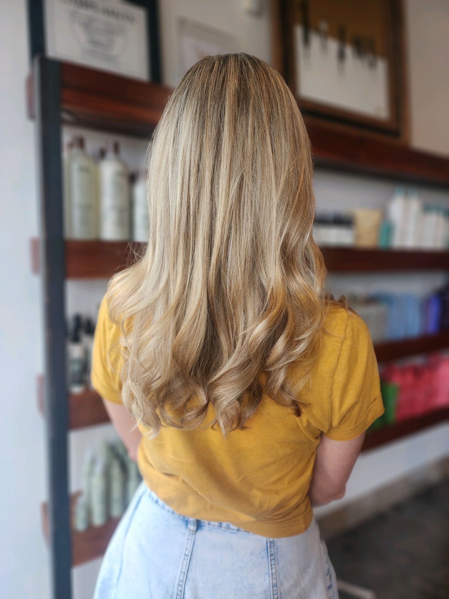 Hair stylist cutting a client's hair with scissors in a salon. The stylist wears a blue sweater and the client has a black cape.