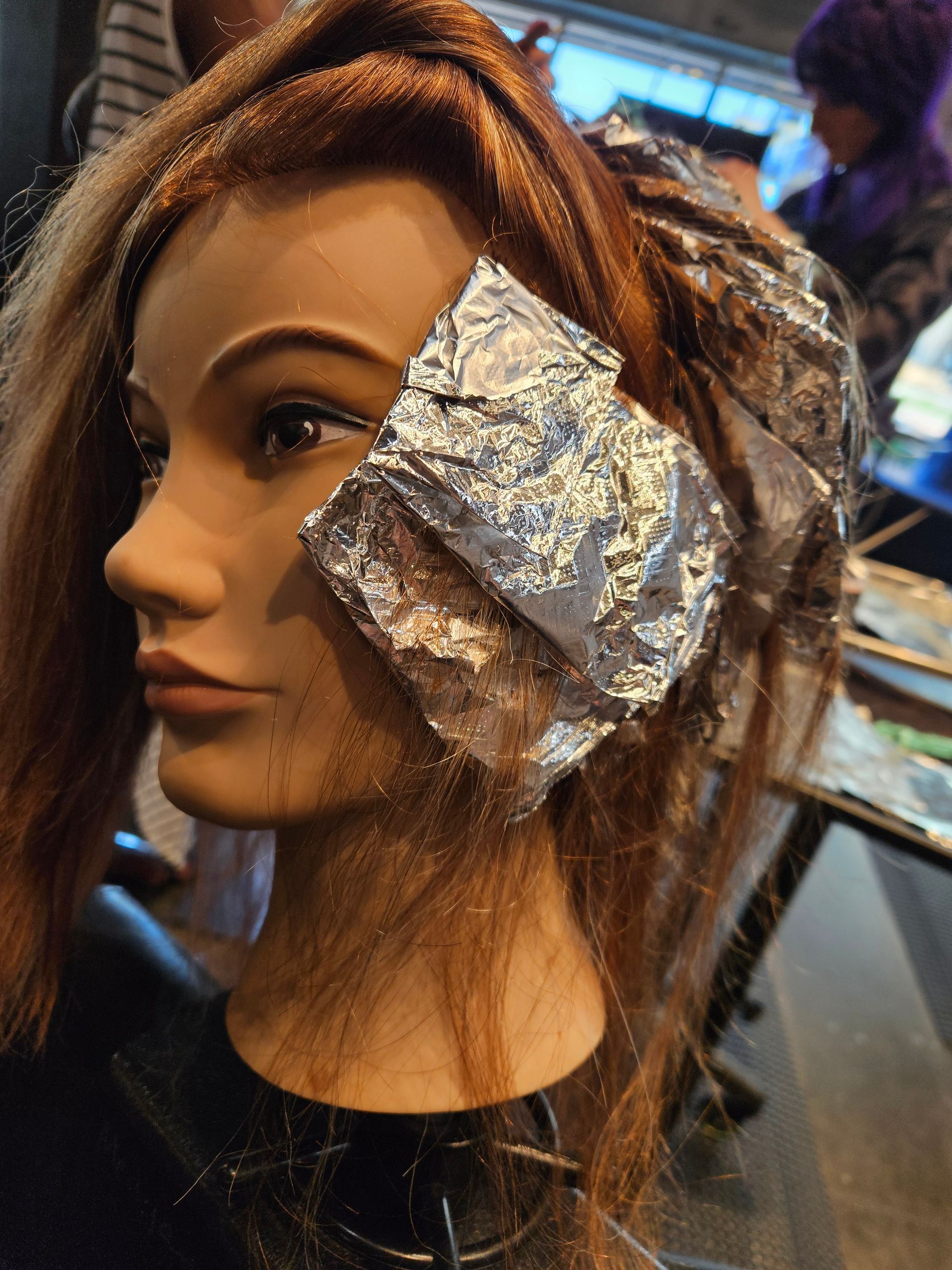 Hair stylist cutting a client's hair with scissors in a salon. The stylist wears a blue sweater and the client has a black cape.