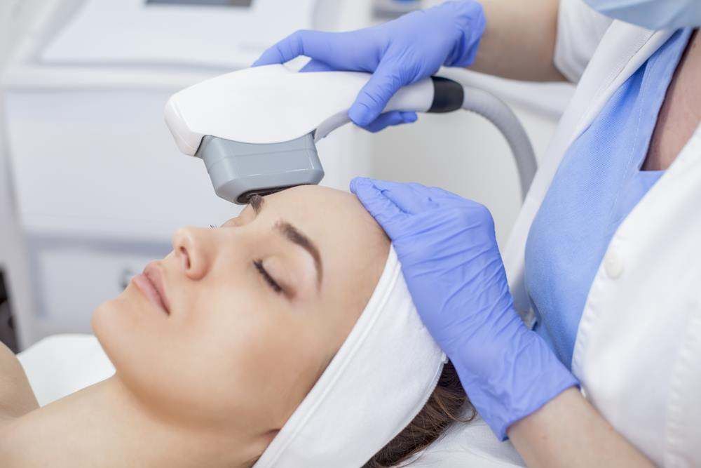 Aesthetician Using a Handheld Device on A Woman’s Forehead — Embrace Cosmetic Clinic in Bundaberg North, QLD