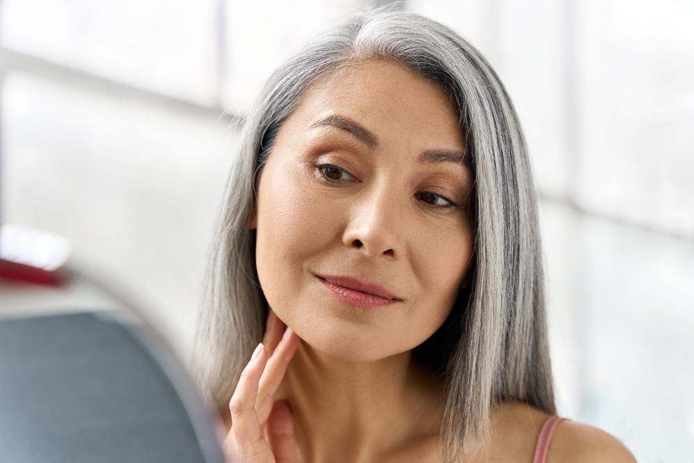Woman Gently Touching Her Jaw While Looking in A Mirror — Embrace Cosmetic Clinic in Bundaberg North, QLD