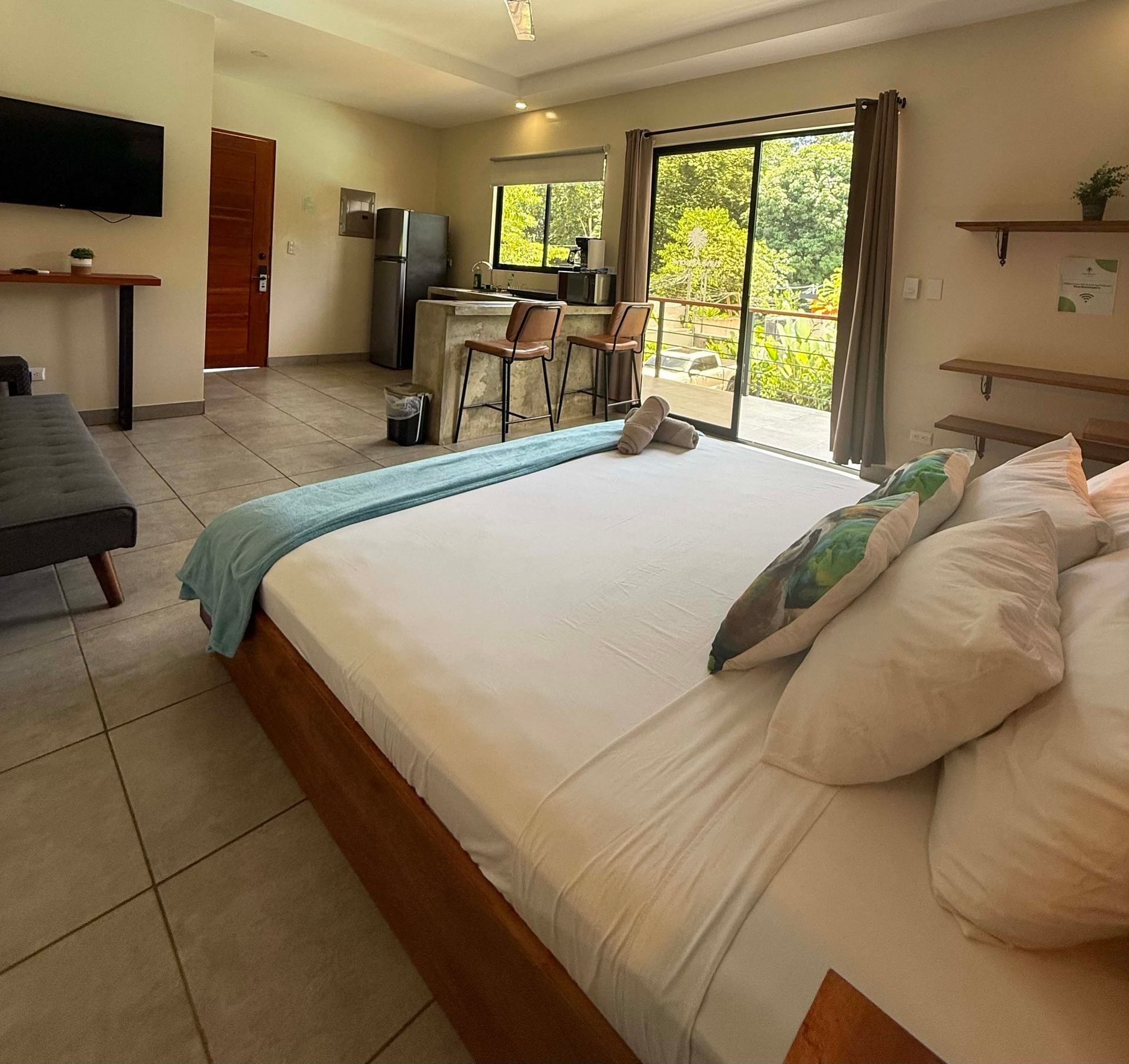Bedroom with bed, kitchenette, and sliding glass door to outside greenery.