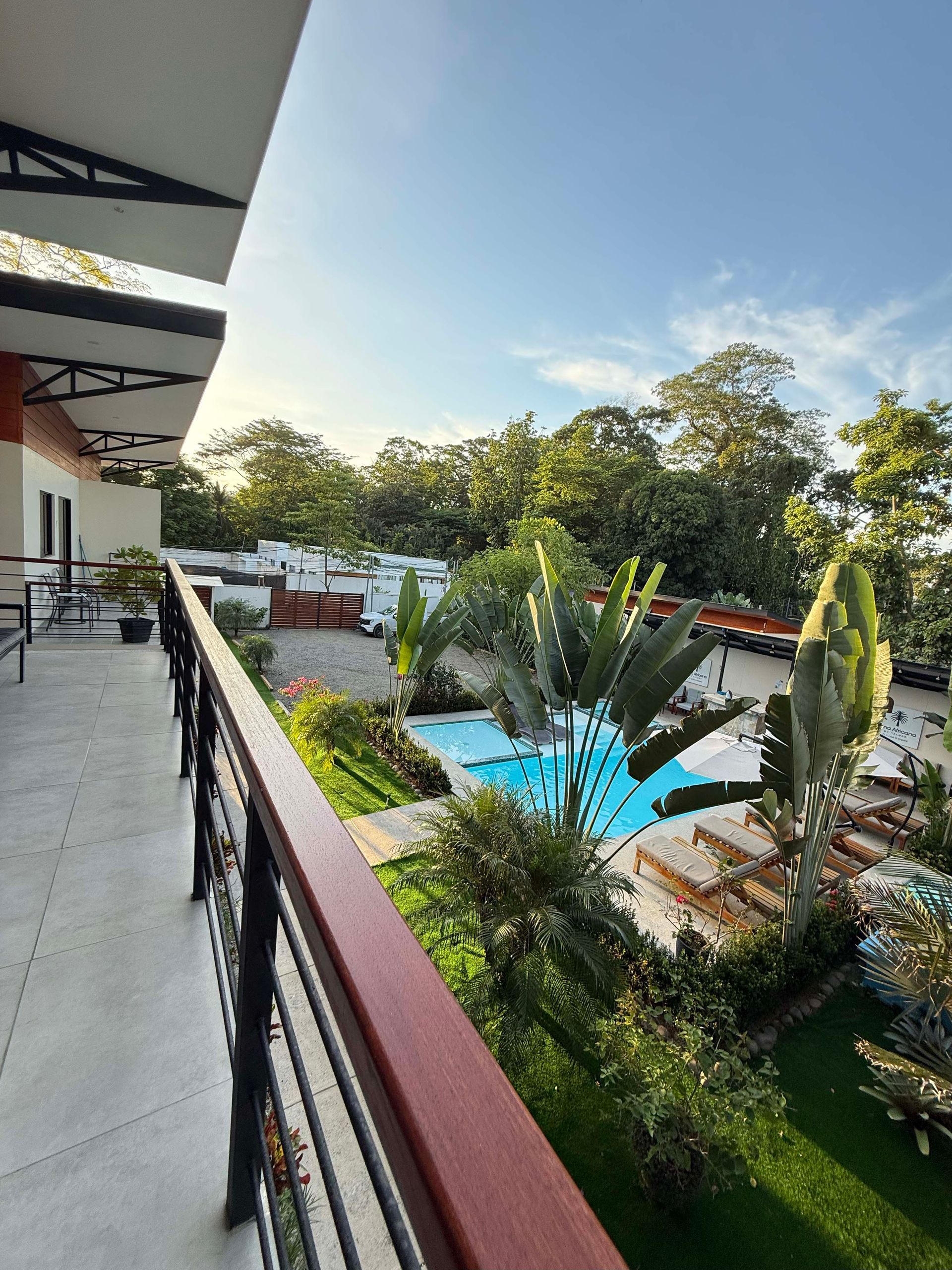 Balcony view of a resort with a pool, green lawn, trees, and blue sky.