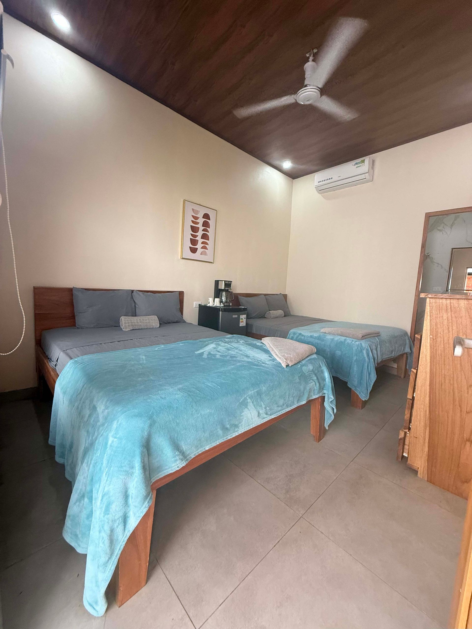 Bedroom with two beds, a small couch, and a ceiling fan; light blue blankets and wooden furniture.