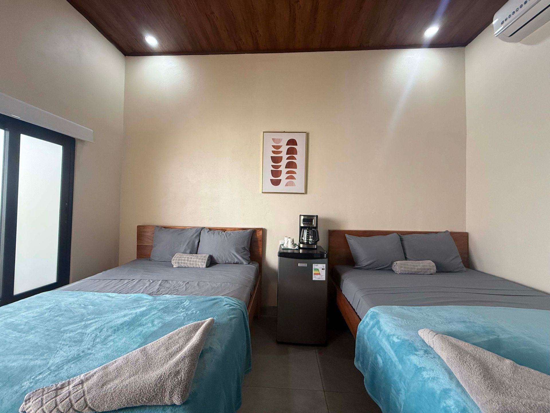 Two beds with teal and gray bedding in a light-colored room with a coffee machine.