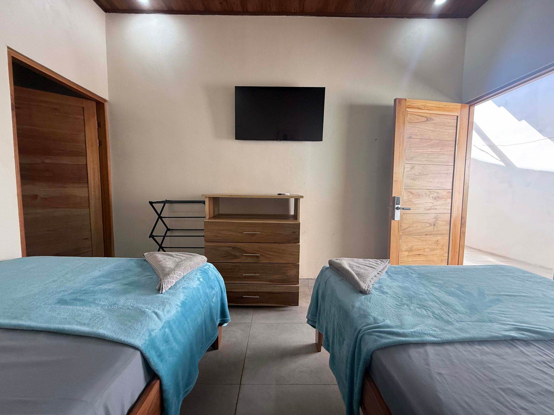 Bedroom with two twin beds, TV, wooden doors, and dresser. Teal blankets, light walls.