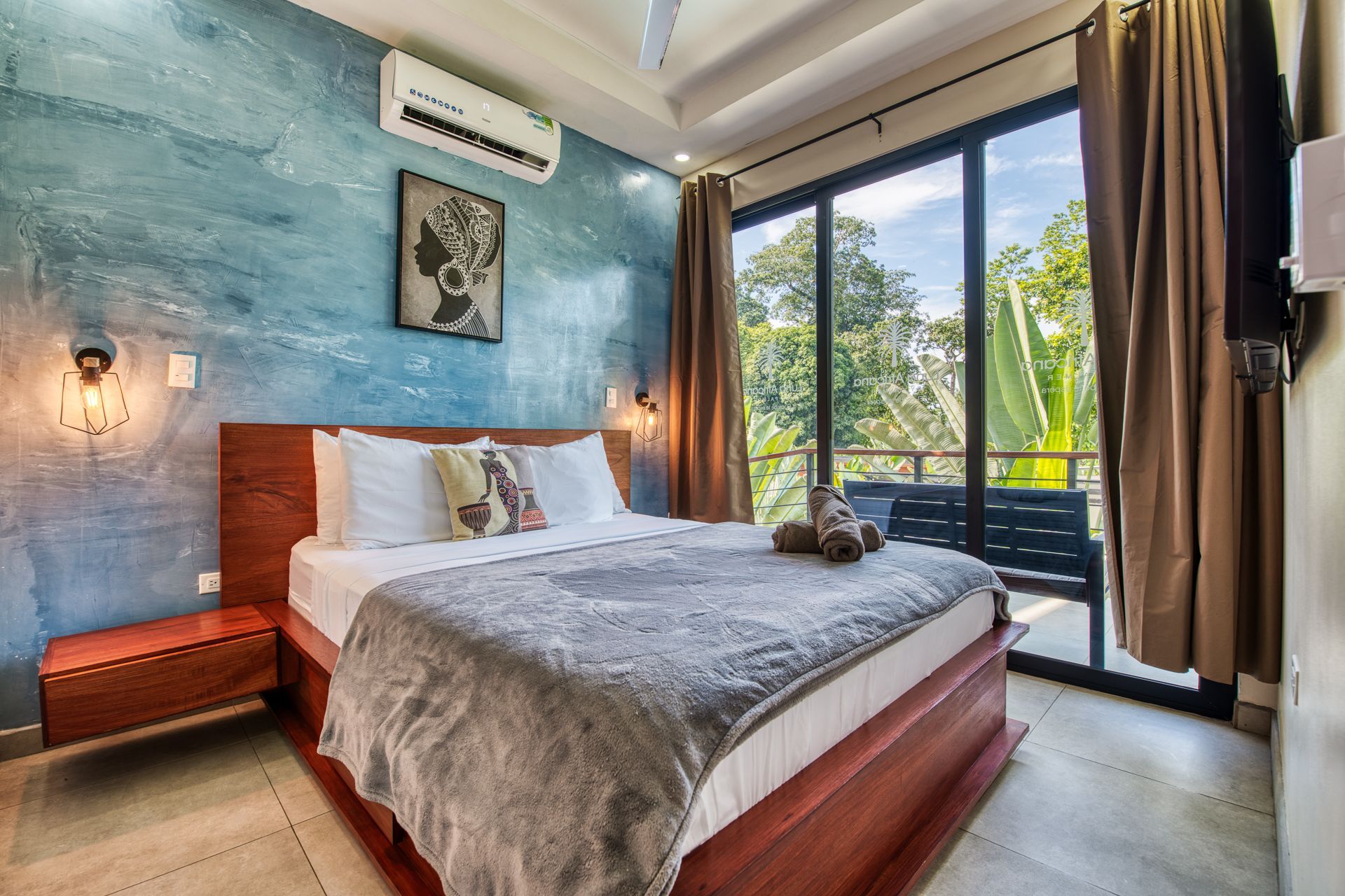 Spacious bedroom with a king bed, blue blanket, and en suite bathroom with a soaking tub.
