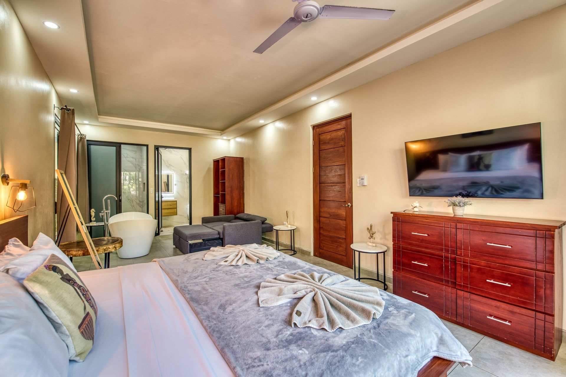 Spacious bedroom with a large bed, bathroom, and a free-standing tub. Neutral walls, with a blue bedspread.