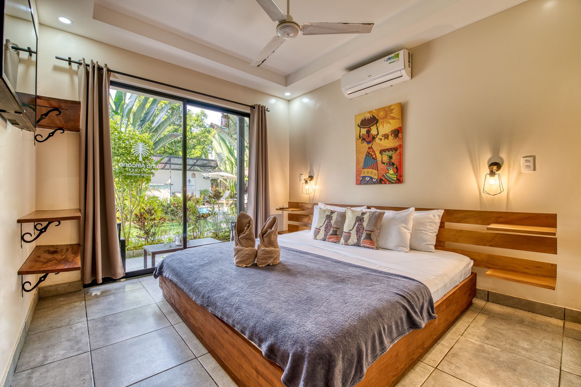 Bedroom with a large bed, open sliding glass door to a garden, ceiling fan, and art.