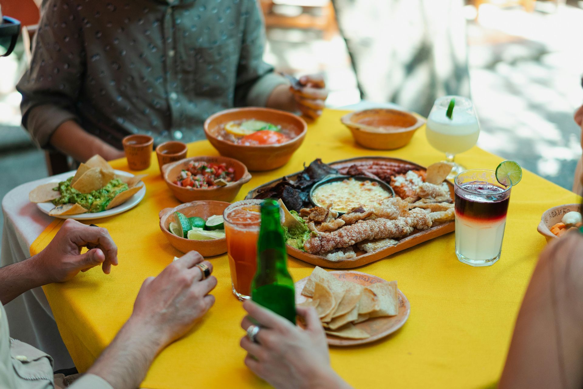 People eating Mexican food at a table with a yellow tablecloth, including various dishes and drinks.