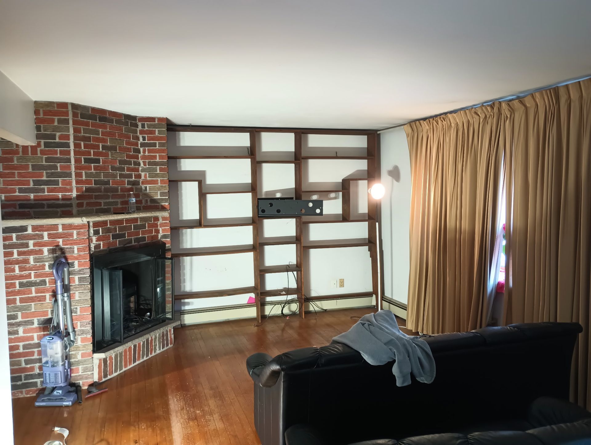 Living room with brick fireplace, built-in shelves, black couch, and gold curtains