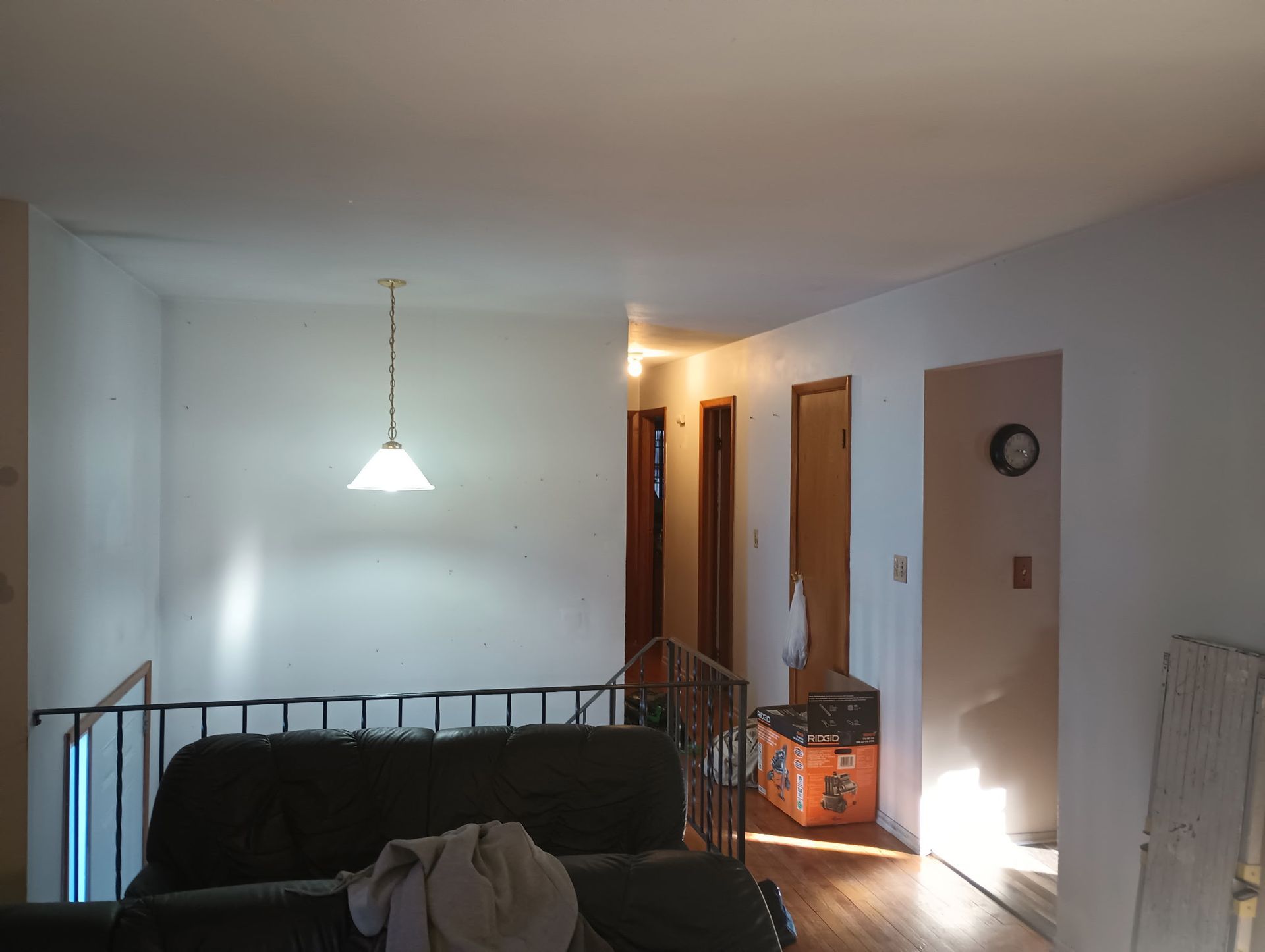 Living room with black couch, hanging lamp, hallway, and sunlight on the wall