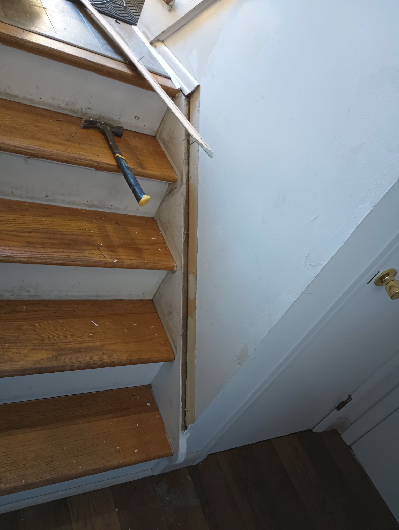 Wooden staircase with white handrail beside a white wall and doorway on dark flooring