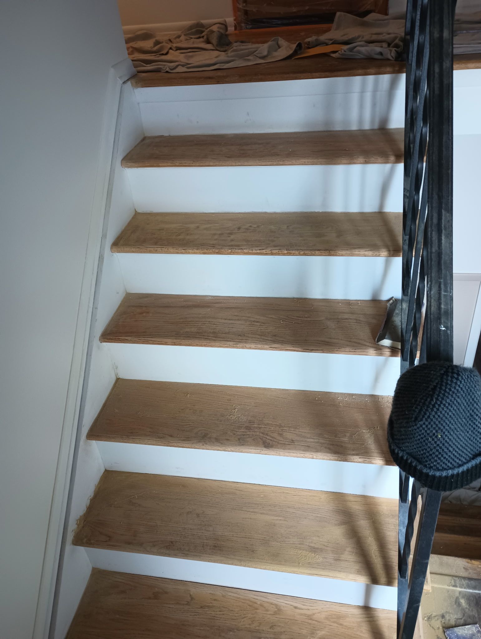 Wooden staircase with white walls and a black handrail, viewed from above.