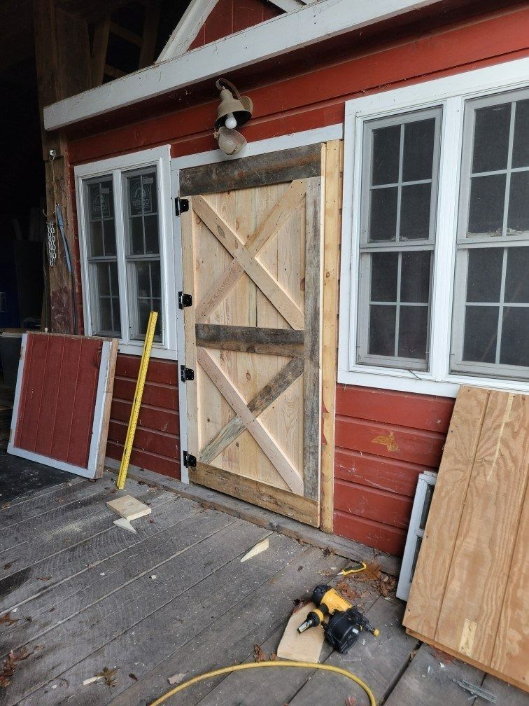 Wooden boarded-up door with tools and window panels leaning against a red exterior wall