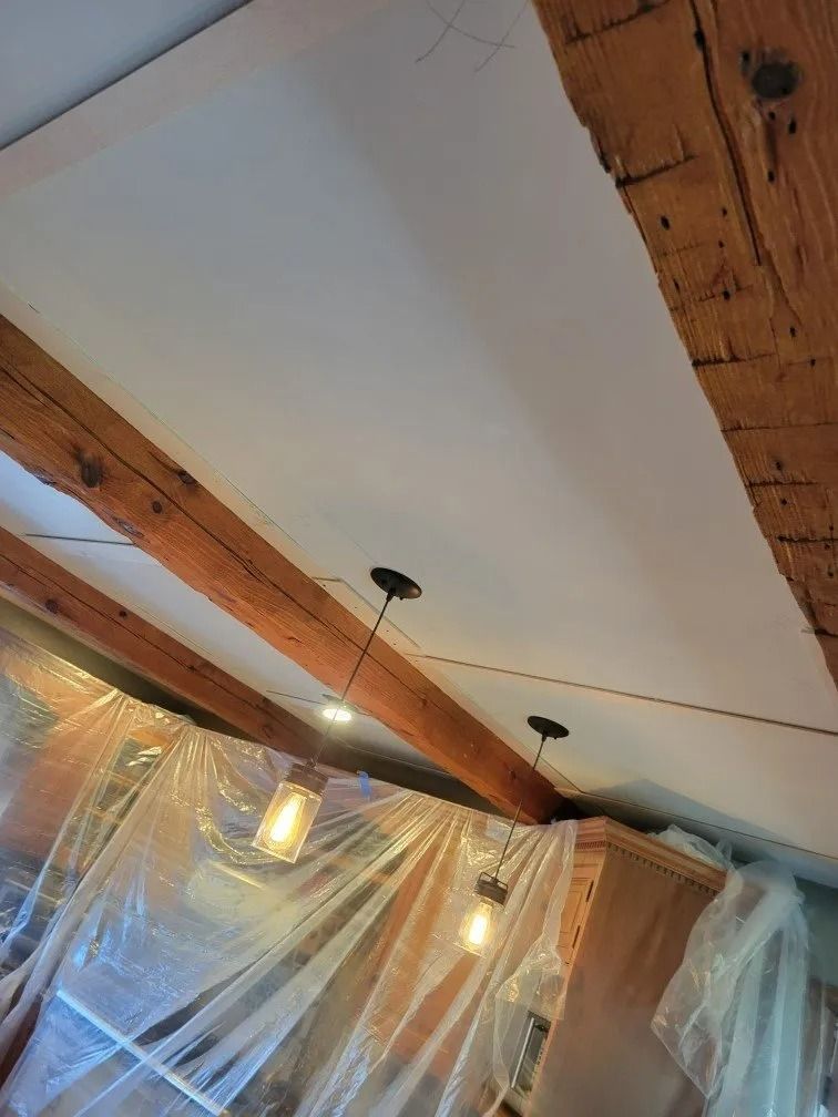 Ceiling with exposed wooden beams, hanging pendant lights, and clear plastic sheeting in a room under renovation