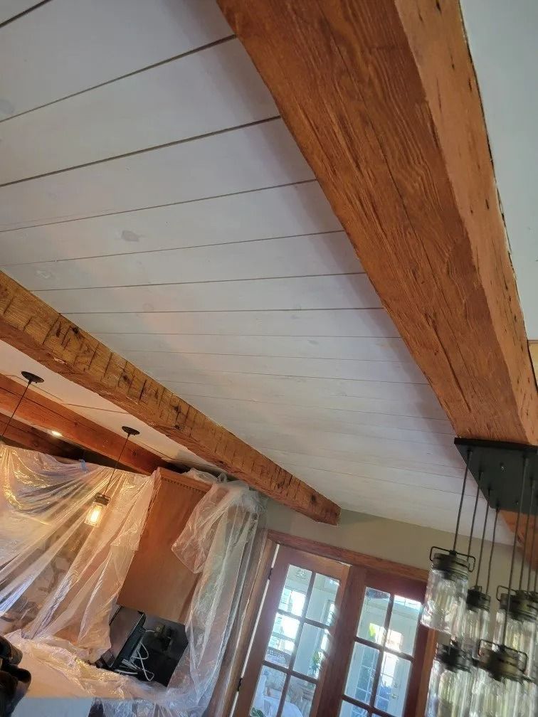 Rustic ceiling with exposed wooden beams and white panels in a room with French doors