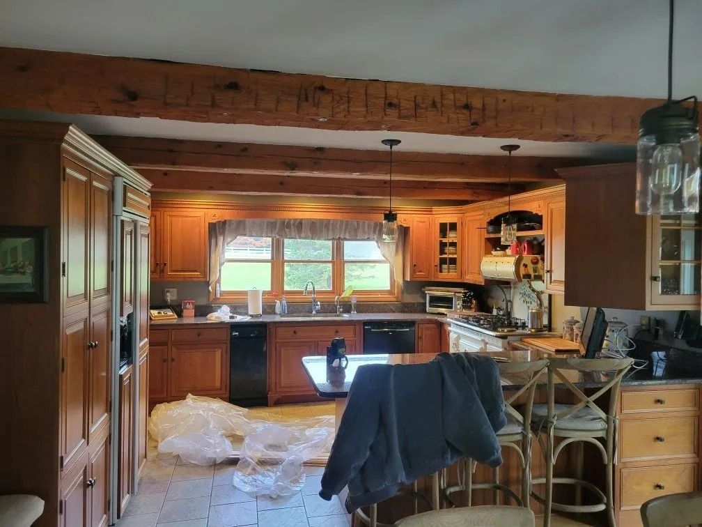 Cluttered kitchen with wooden cabinets, island, and chairs, seen mid-cleanup with plastic covering the floor.