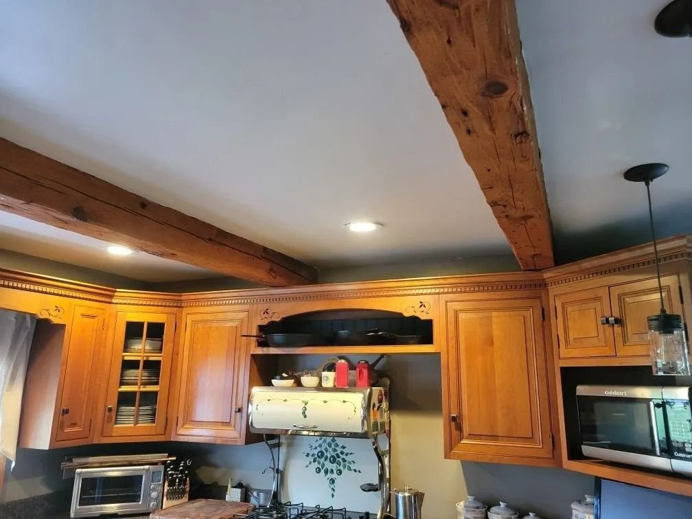 Kitchen with wooden beams, oak cabinets, and stainless appliances under warm ceiling lights