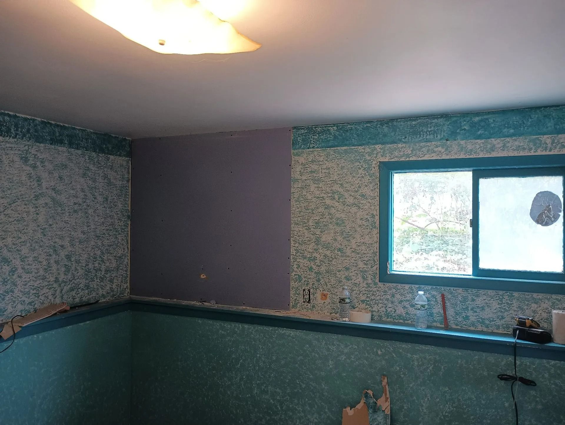 Small room with teal patterned walls, a window, and a ceiling light.