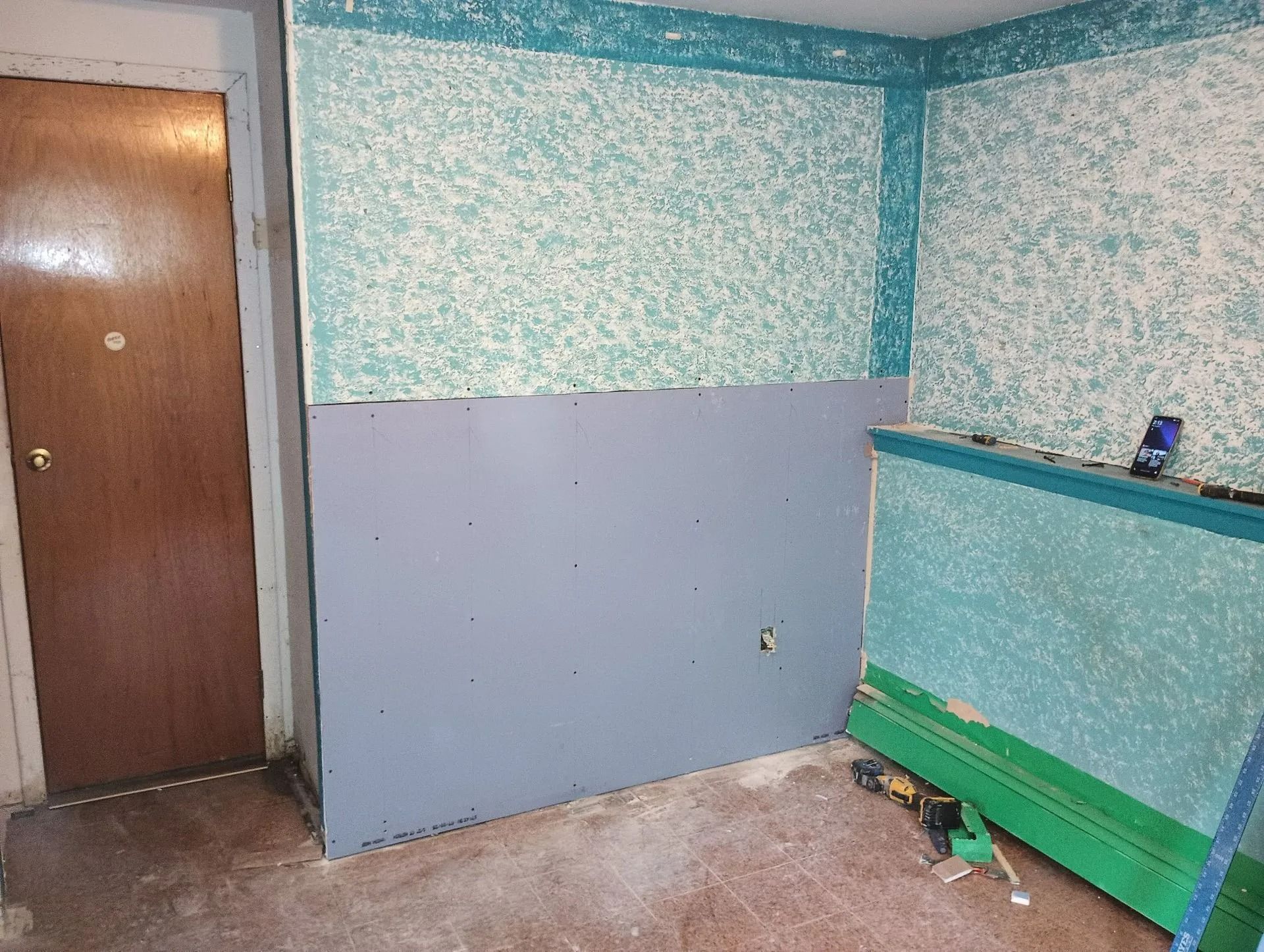 Small room with a brown door, teal-speckled walls, and a green bench along the right side.