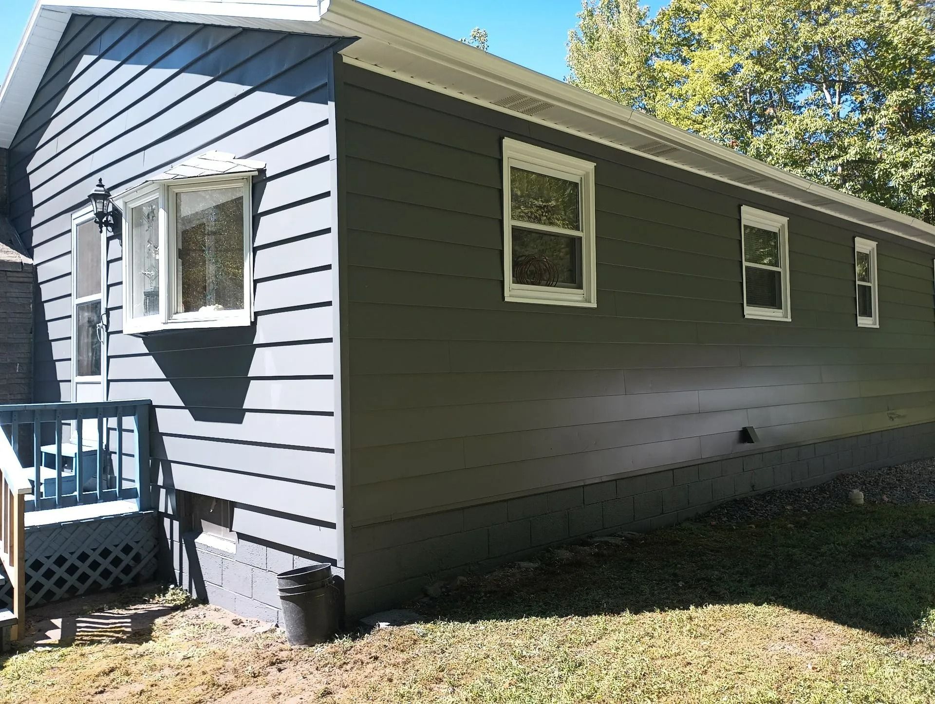 Side view of a gray house with white-trimmed windows, blue porch railing, and grassy yard