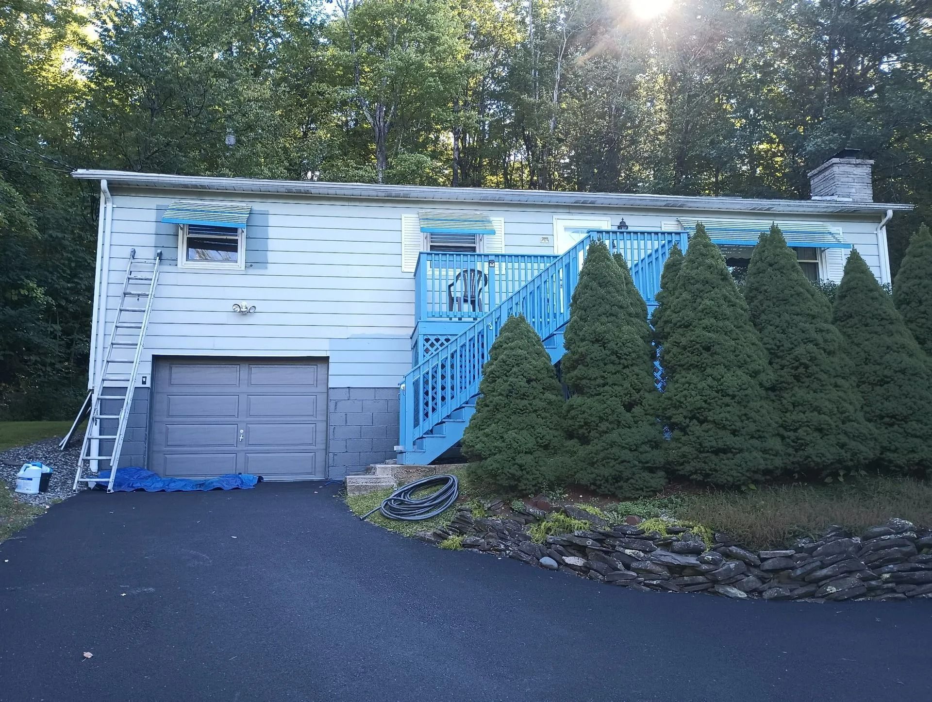 White house with blue stairs, garage, and row of evergreen shrubs beside a driveway at dusk