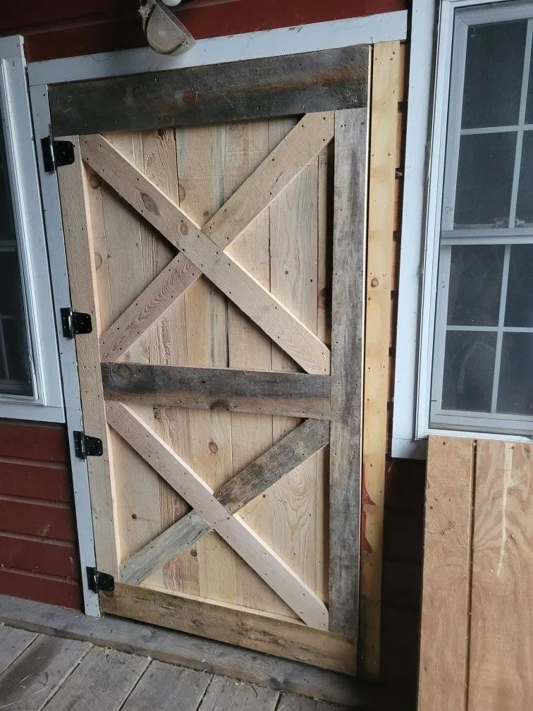 Wooden barn-style door with X-bracing, framed beside windows on a house exterior
