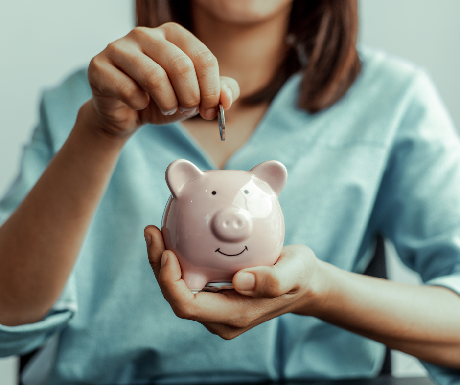 Hands place a coin into a pink piggy bank against a soft blue background.