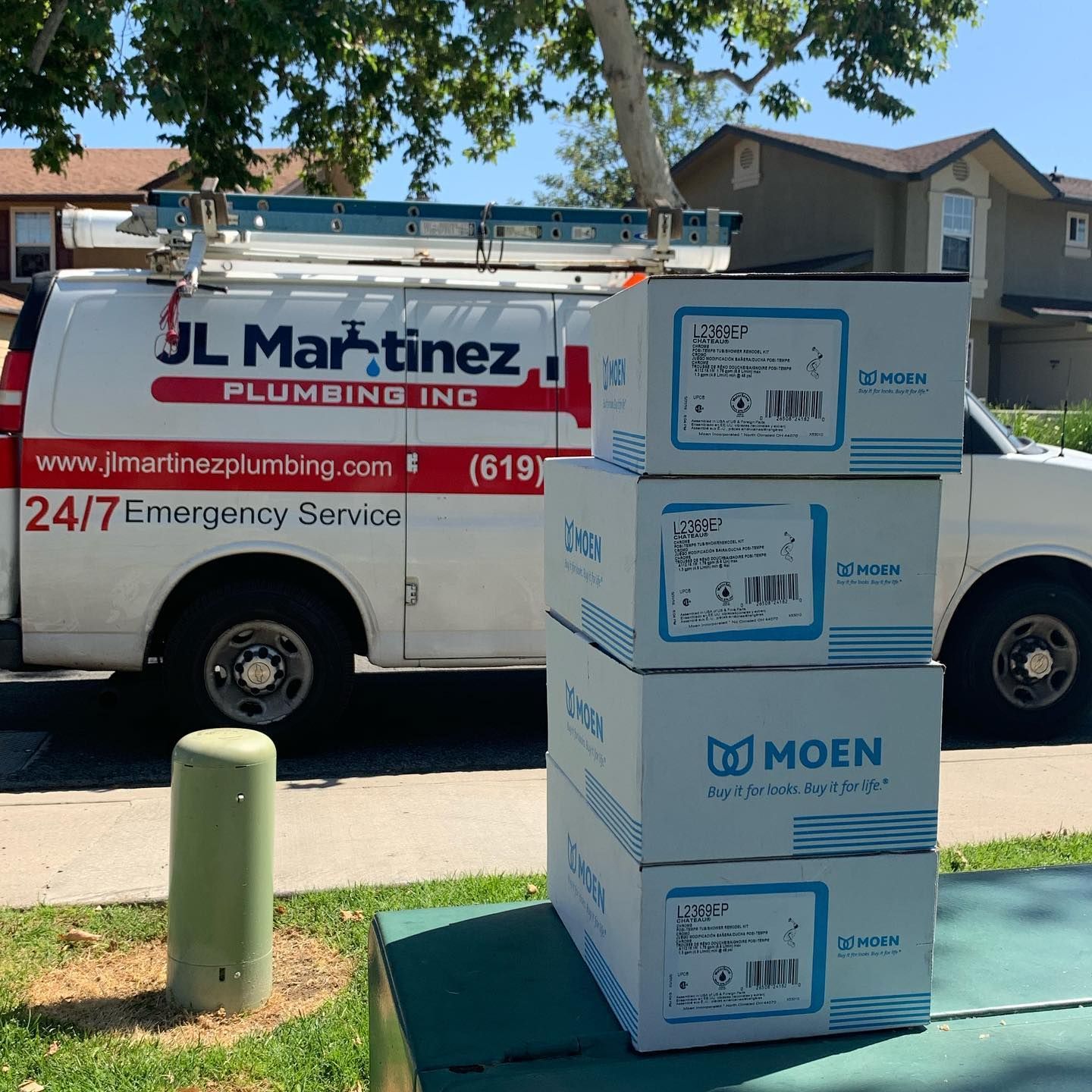 Plumber service van behind stacked Moen boxes on a sunny suburban street