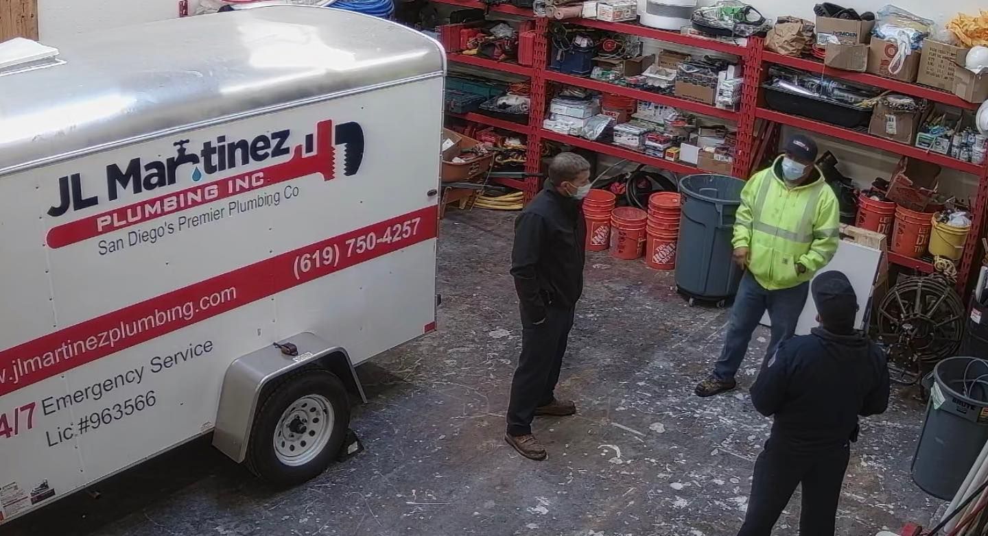Delivery van and three people talking in a snowy warehouse yard beside red shelving and crates.