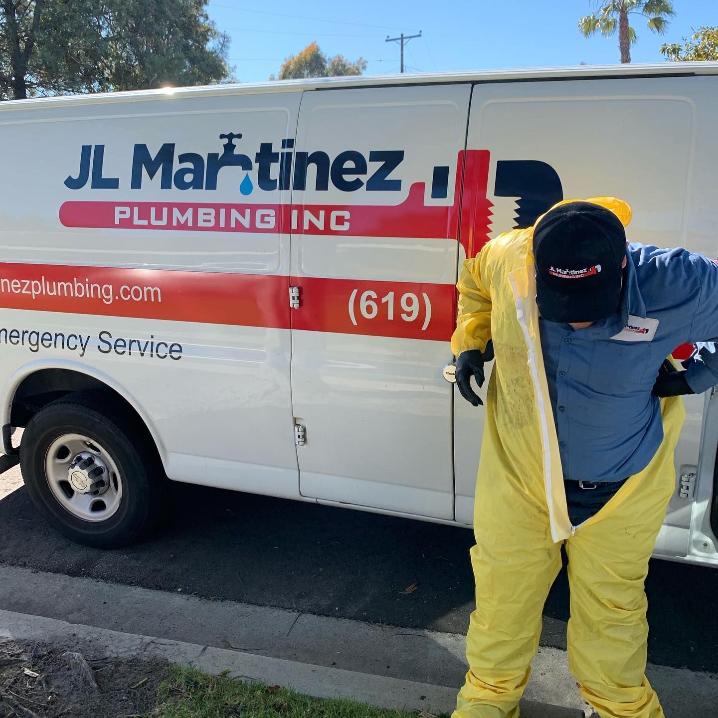 Technician in yellow hazmat suit in front of JL Martinez Plumbing van on a sunny street