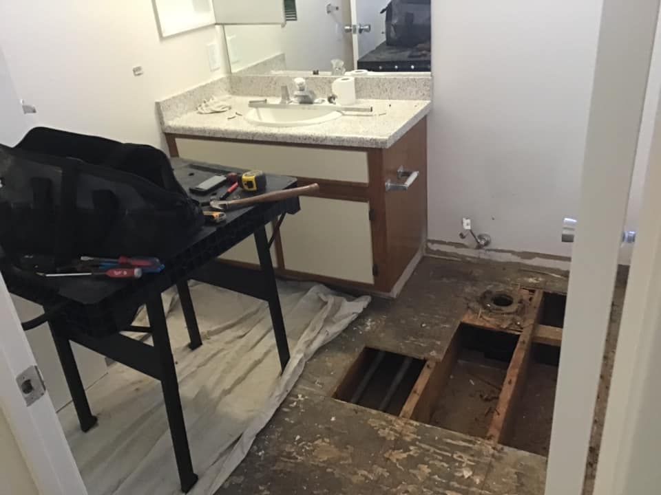 Bathroom with a vanity sink and a large open floor hole exposing plumbing, next to a black chair.